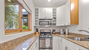 A kitchen with white cabinets, a stainless steel stove, a microwave, and a granite countertop. - Carmel Romantic Escape for 2 (Carmel)