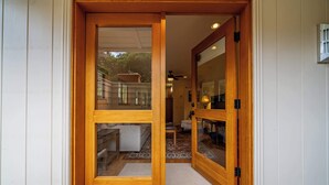 A wooden door with glass panels leading to a room with a patterned rug and a white chair. - Carmel Romantic Escape for 2 (Carmel)