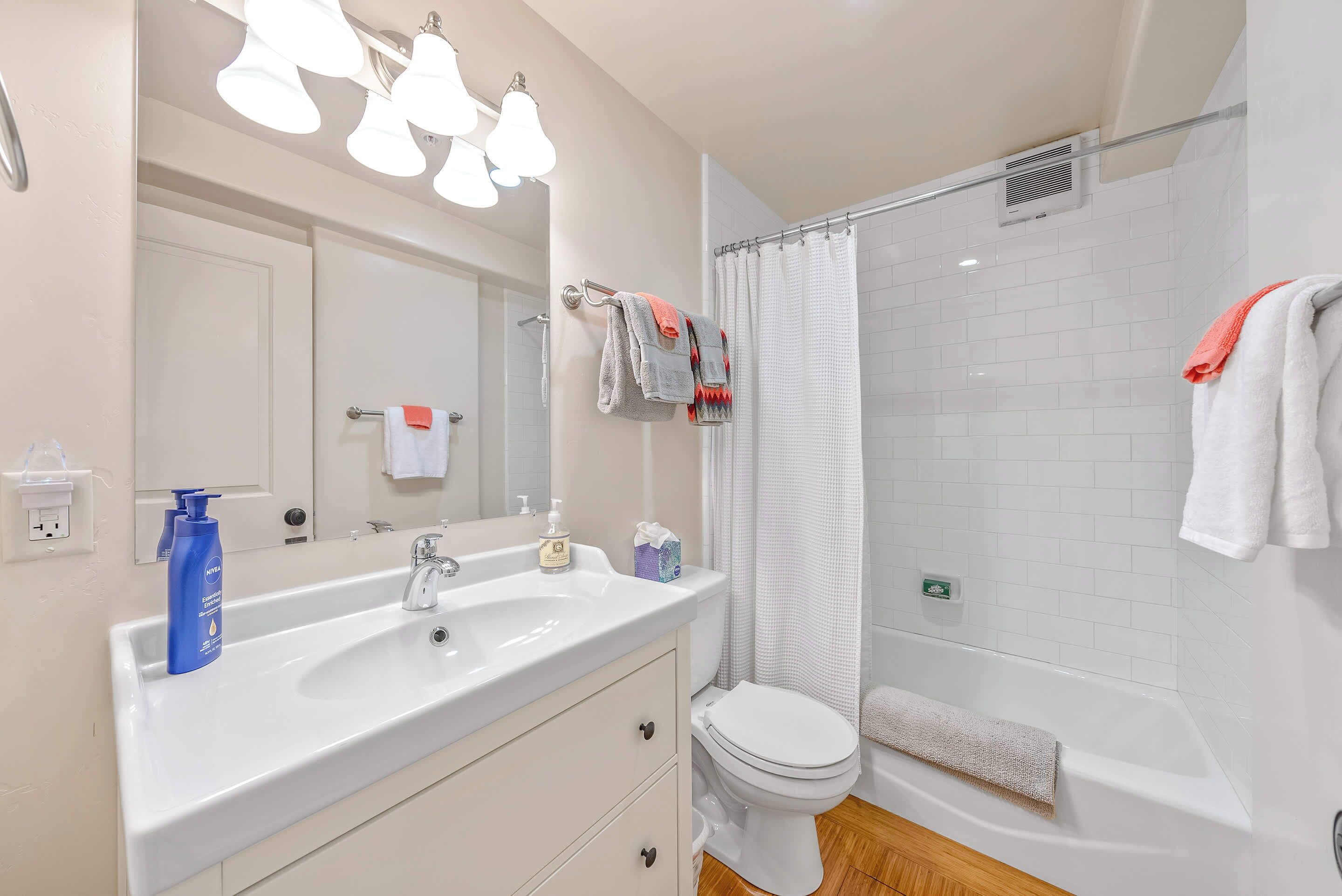 A bathroom with a white sink, mirror, and toilet. There are towels hanging on a rack and a shower curtain.