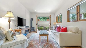 A living room with a sofa, a coffee table, a TV, and a window with a view of greenery. - Carmel Romantic Escape for 2 (Carmel)