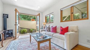 A living room with a sofa, a glass coffee table, a rug, and a view of greenery through a door. - Carmel Romantic Escape for 2 (Carmel)