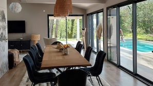 Ein moderner Essbereich mit einem Holztisch und schwarzen Stühlen, großen Fenstern mit Blick auf einen Pool und einer Decke mit freiliegenden Balken.