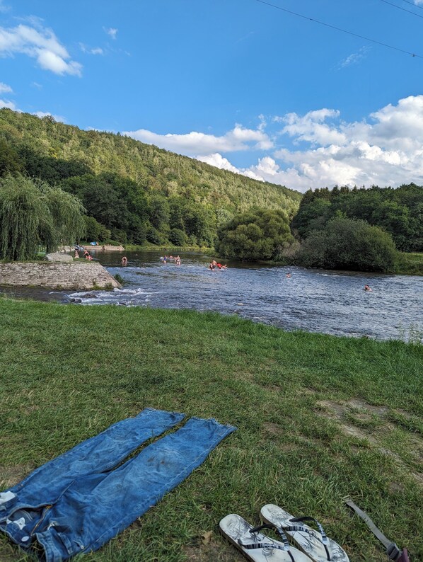 A grassy area with a river, a blue tarp, and a pair of shoes. - Gîte des Genêts en terrasses (Bièvre)