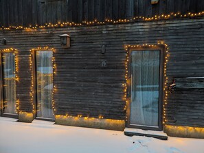 A wooden building with numbered doors, likely a hotel or guesthouse, with string lights along the edges. - Gîte des Genêts en terrasses (Bièvre)