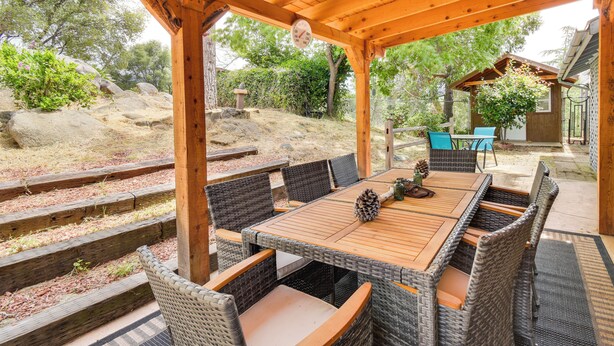 A covered patio with a wooden table and wicker chairs, surrounded by stone steps and greenery. - Yosemite Wellbeing Retreat on 5 Acres w/ Mtn Views (Ahwahnee)
