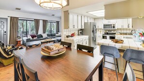 A modern kitchen with white cabinets, a central island, and a dining area with a wooden table and chairs. - Yosemite Wellbeing Retreat on 5 Acres w/ Mtn Views (Ahwahnee)