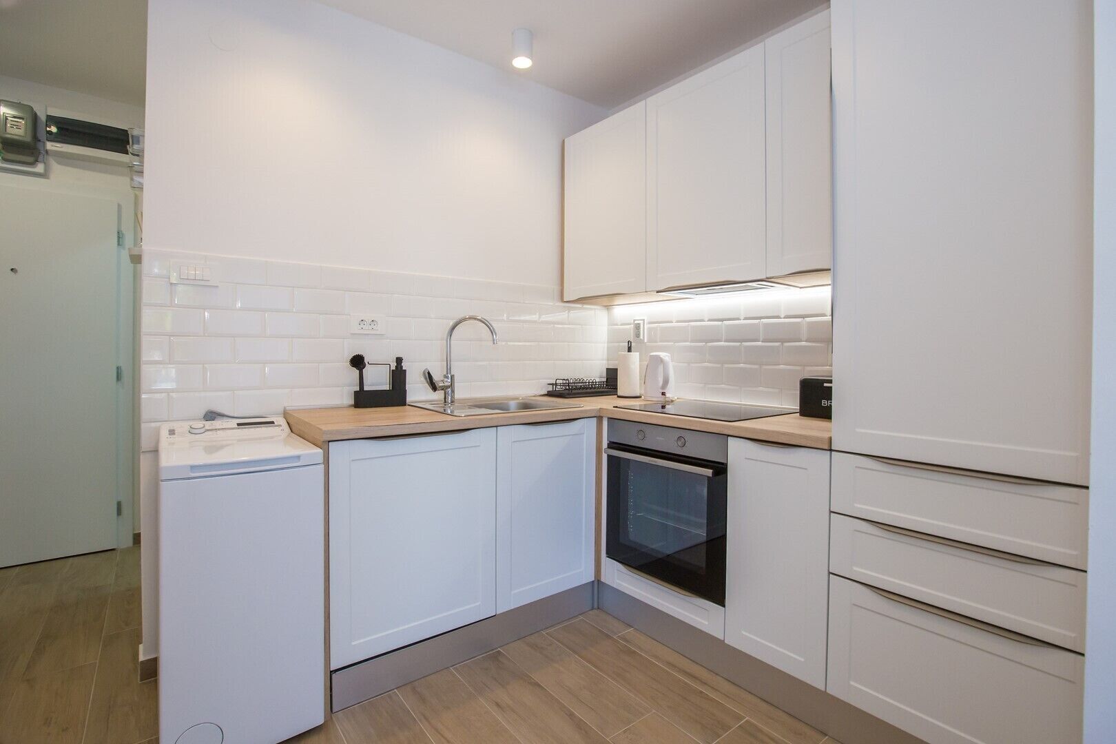 Una cocina compacta con muebles blancos, horno empotrado y lavavajillas.