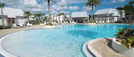A swimming pool with lounge chairs and palm trees, surrounded by buildings with white roofs.