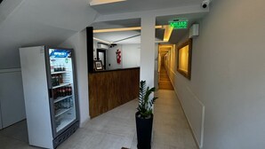 Un couloir d’hôtel avec un comptoir de réception, un réfrigérateur rempli de boissons et une plante en pot.