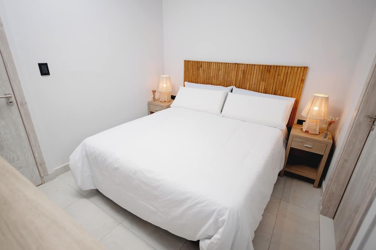Een keurig opgemaakt bed met witte lakens, twee nachtkastjes met lampen en een houten hoofdeinde.