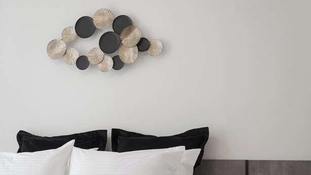 Une chambre à coucher moderne avec un lit, une literie noire et blanche, une tête de lit en bois, une table de chevet avec une lampe, et une œuvre d’art murale au-dessus du lit.