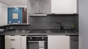 Une cuisine moderne avec un plan de travail noir, des meubles gris, un four encastré et un évier.