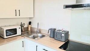 A modern kitchen with a microwave, toaster, sink, and electric stove. - Leeds City Escape - Stylish Apartment (Leeds)