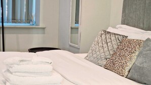 A neatly made bed with white linens and a stack of folded towels. - Leeds City Escape - Stylish Apartment (Leeds)