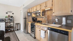 A modern kitchen with wooden cabinets, stainless steel appliances, and a coffee-themed wall decal. - The Nautical Nook Charming Walk-in Condo for 4! (Branson)