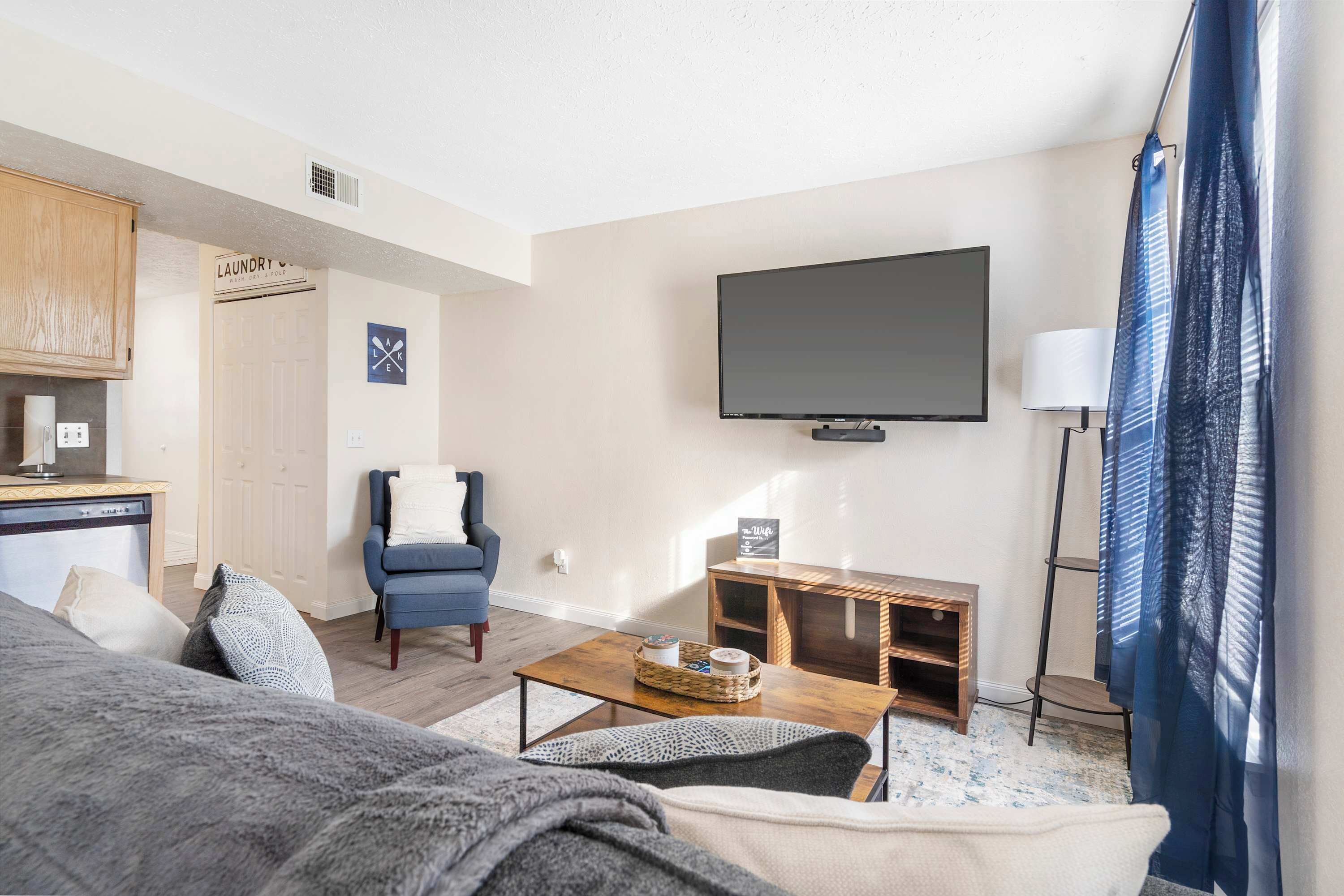 Una sala de estar con sofá, mesa de centro, televisor, silla, pequeña mesita de madera y un letrero de lavandería.