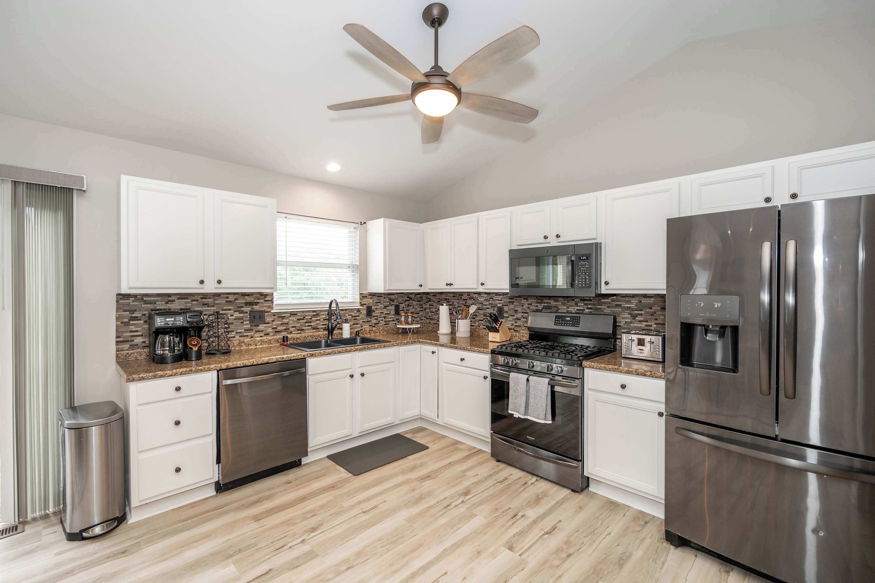A modern kitchen with white cabinets, stainless steel appliances, a microwave, a stove, and a ceiling fan.