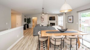 A modern living room with a gray sofa, a wooden dining table with chairs, a ceiling fan, and a large window. - Poolside Paradise Near the Ark (Walton)