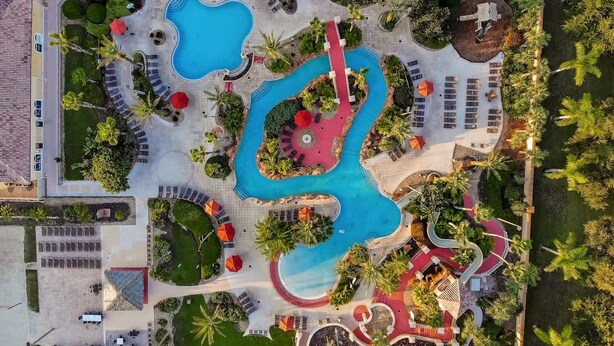 An aerial view of a resort with multiple swimming pools, sun loungers, and palm trees. - Mickeys Oasis At Regal Palms (Davenport)