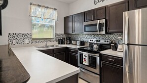A modern kitchen with dark wooden cabinets, stainless steel appliances, and a white countertop. - Mickeys Oasis At Regal Palms (Davenport)