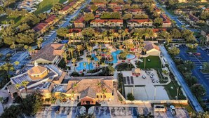 An aerial view of a residential area with a central swimming pool, multiple buildings, and a large parking lot. - Mickeys Oasis At Regal Palms (Davenport)