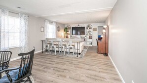 A dining area with a wooden table and chairs, a kitchen island with bar stools, and a TV. - Arkstone Retreat - 3 in 1! Only 4 min to the Ark! (Williamstown)