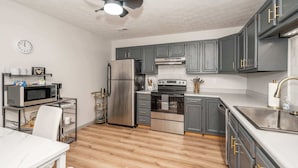 A modern kitchen with grey cabinets, stainless steel appliances, and a white ceiling fan. - Arkstone Retreat - 3 in 1! Only 4 min to the Ark! (Williamstown)