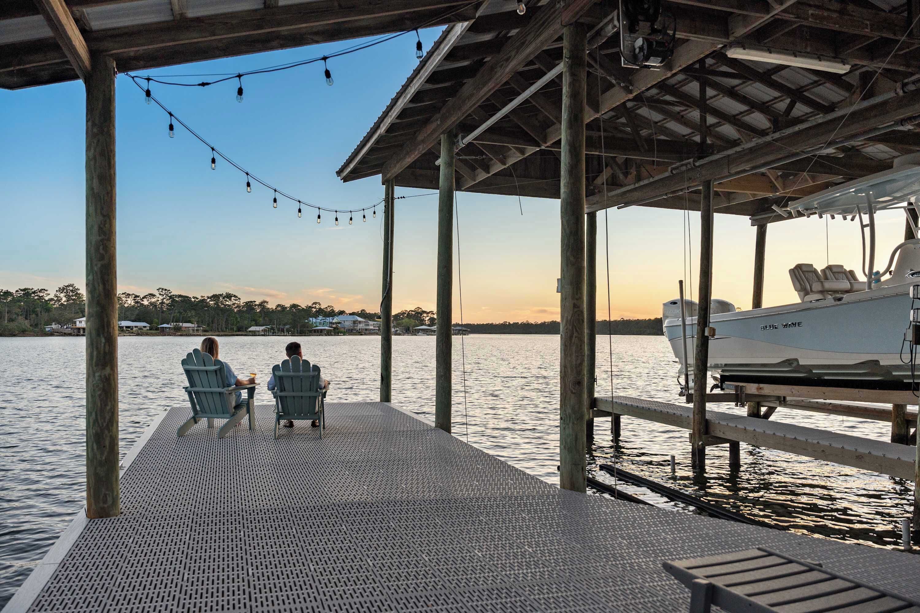 A wooden dock with two chairs and a table, overlooking a calm body of water with a boat docked nearby.