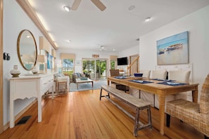 A spacious living area with a wooden floor, a dining table set for four, a large mirror, and a painting of boats on the wall.