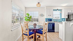 Una cocina moderna con armarios blancos, salpicadero azul y un comedor con mesa redonda y sillas con acolchado azul.