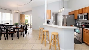 A modern kitchen with a central island, wooden stools, and stainless steel appliances.