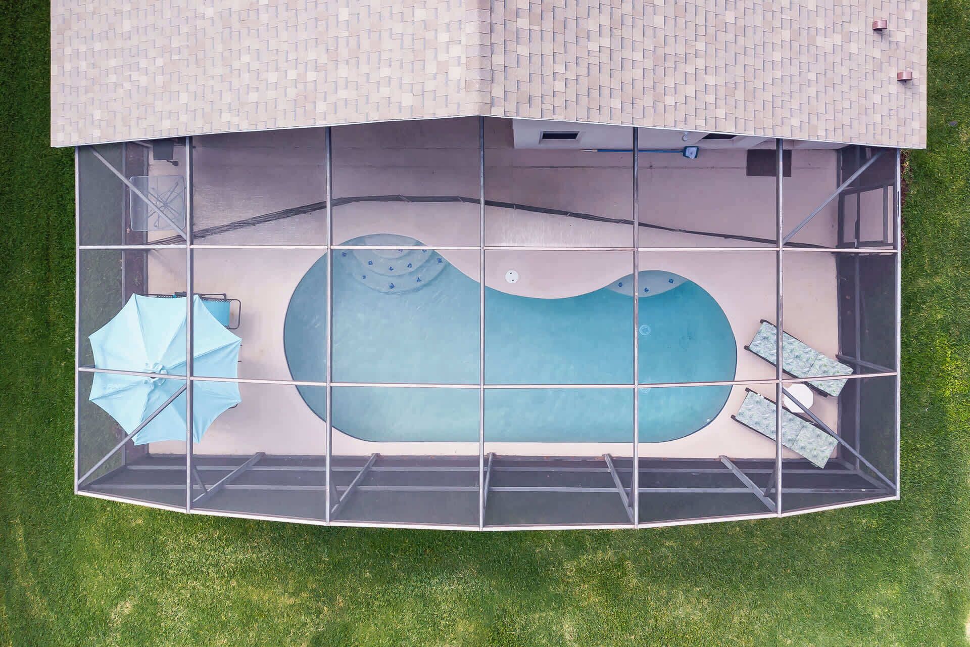 An aerial view of a swimming pool with a tiled deck, a blue umbrella, and lounge chairs.