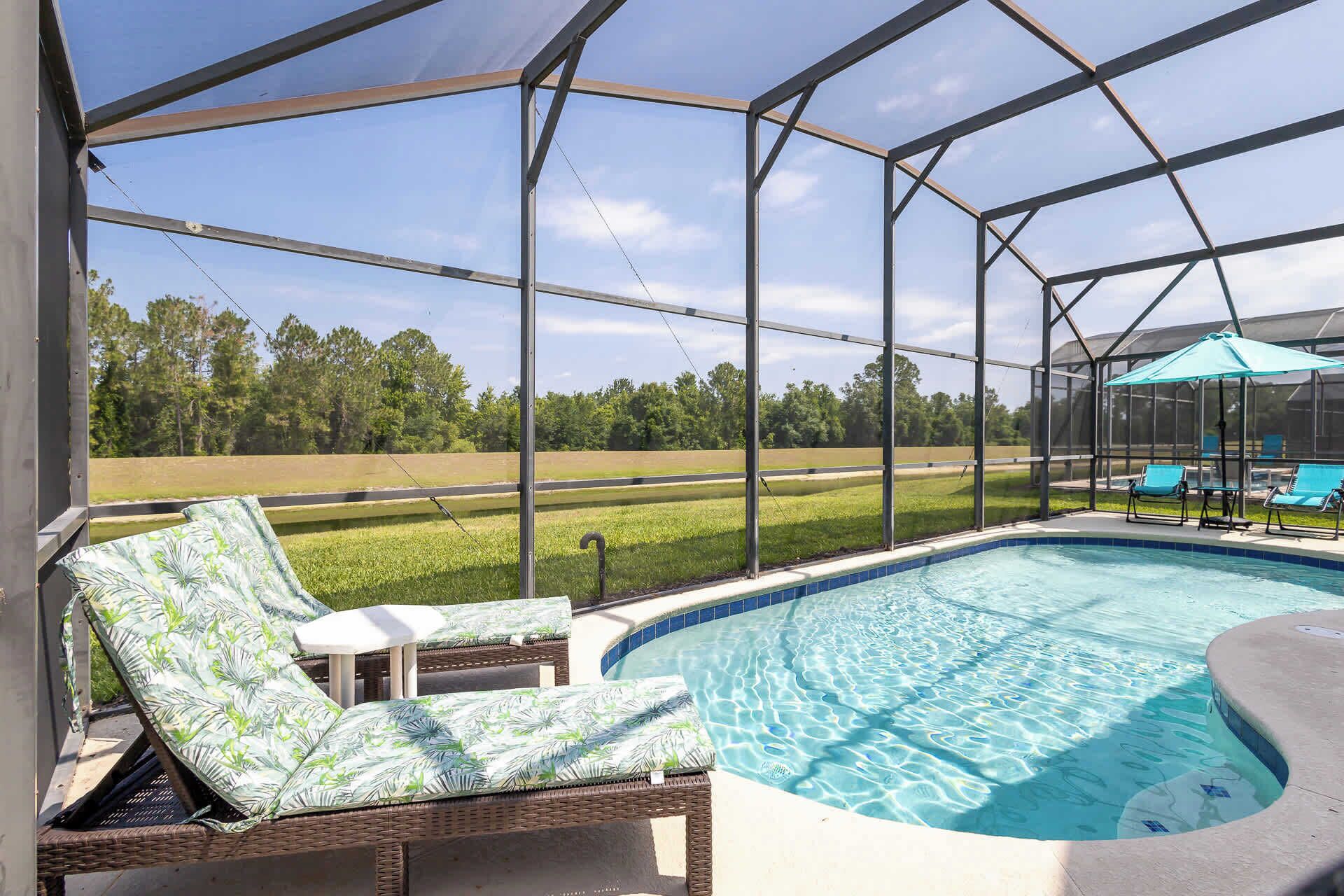 A screened-in outdoor area with a swimming pool, lounge chairs, and a view of a grassy field.