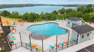 Una piscina con borde curvo, rodeada por una valla y vista al lago de fondo.