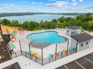 A swimming pool with a curved edge, surrounded by a fence, and a view of a lake in the background. - Lakefront Oasis Amazing Views! (Kimberling City)