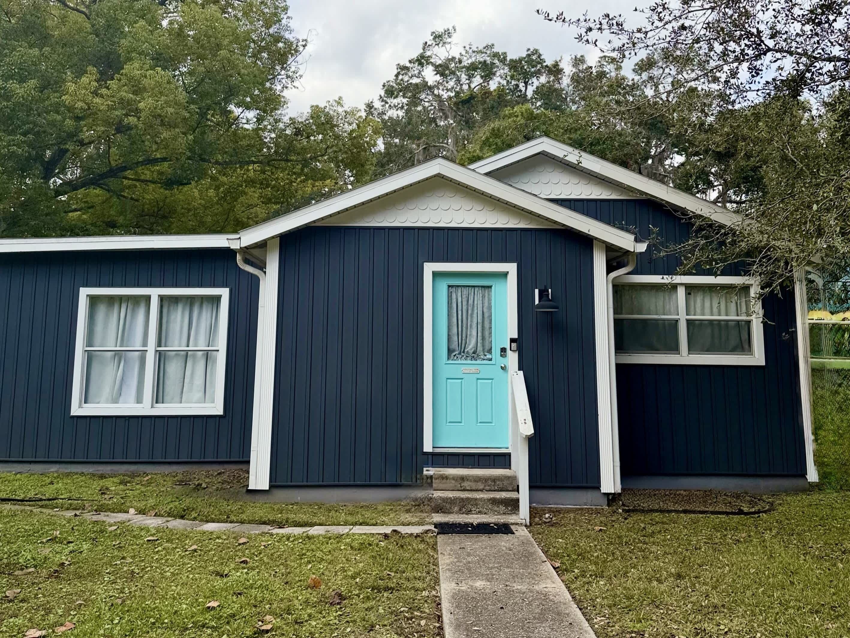 A small, single-story house with a dark blue exterior, a white door, and a small porch.