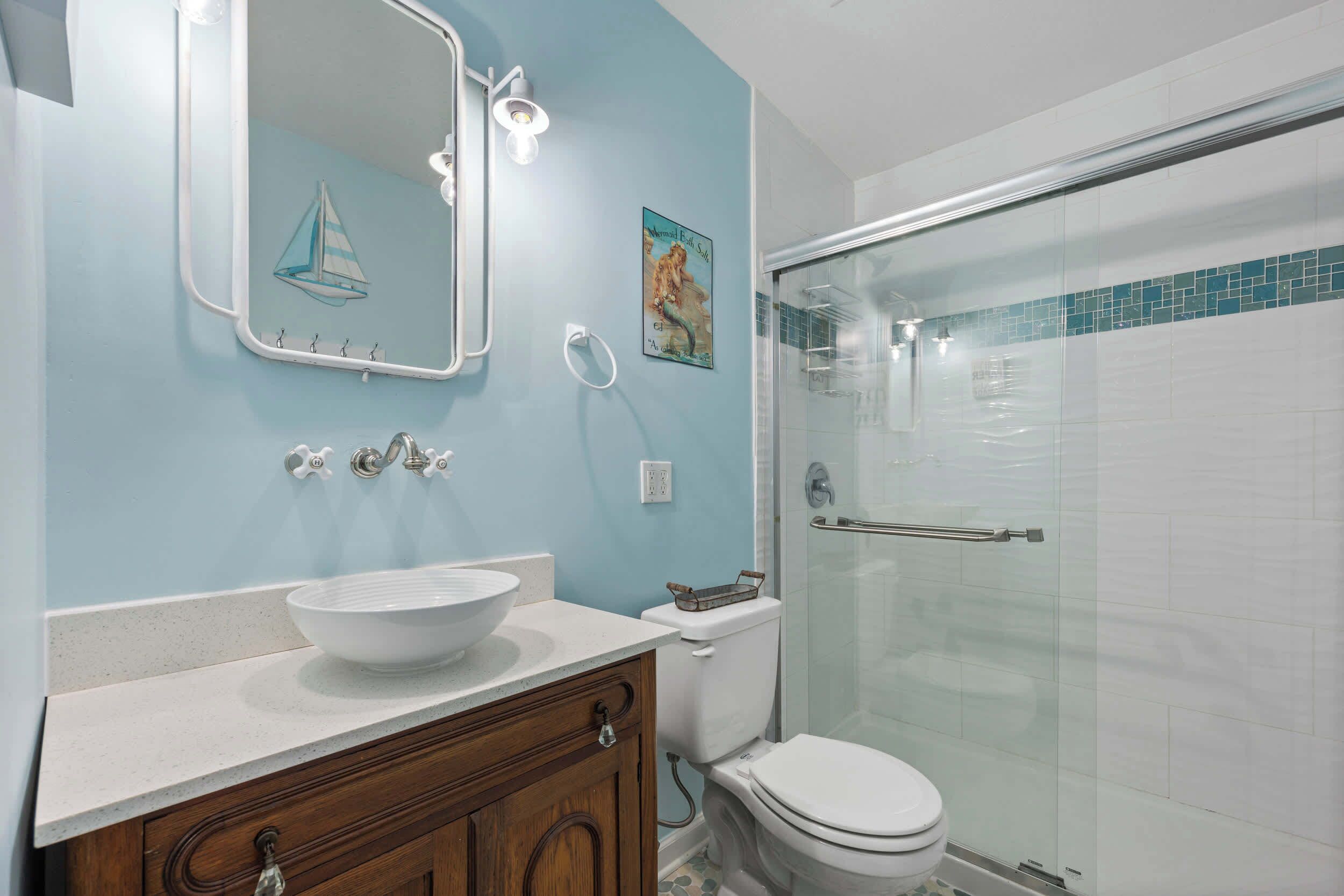A bathroom with a sink, mirror, toilet, and glass shower enclosure.