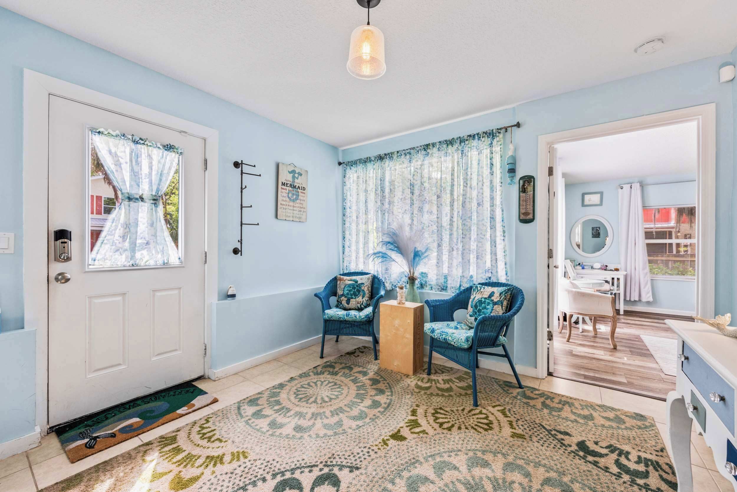 Una habitación con una puerta blanca, paredes azules, dos sillones azules, una mesita de madera y una alfombra estampada.