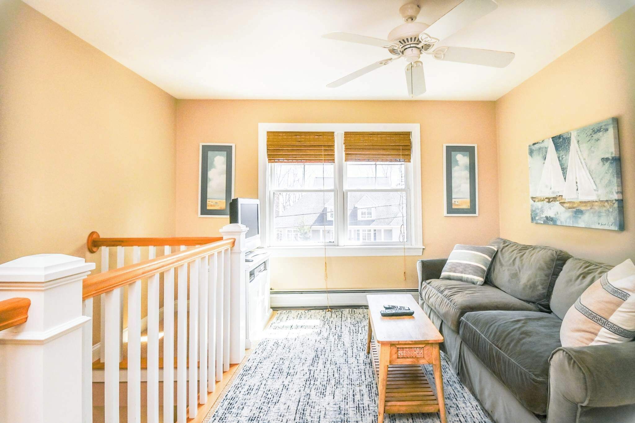A living room with a gray sofa, a wooden coffee table, a ceiling fan, and a window with blinds.
