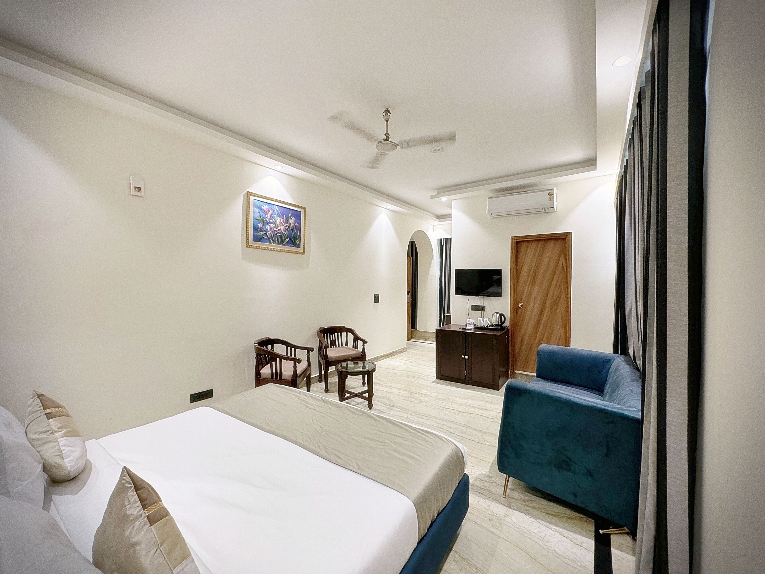 Una habitación de hotel con cama, un sillón azul, un escritorio y un televisor de pantalla plana, además de un ventilador de techo.