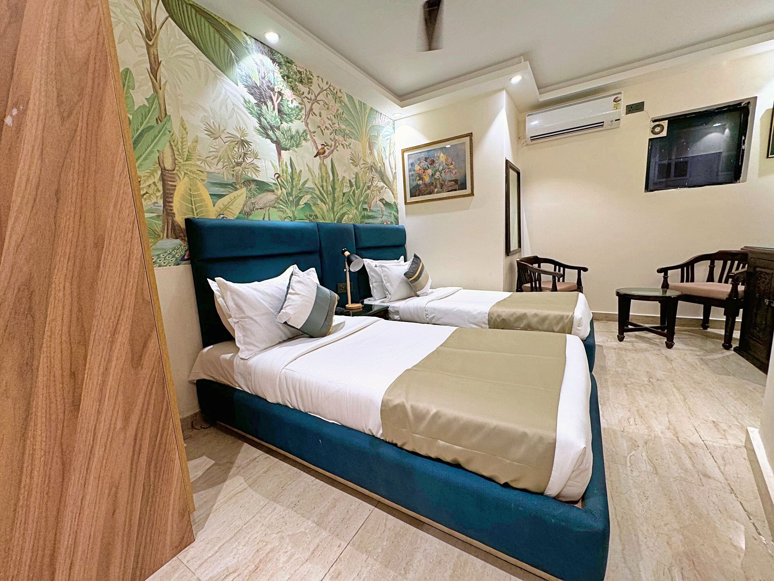 A hotel room with two beds, a mural, a painting, a desk, and a chair.