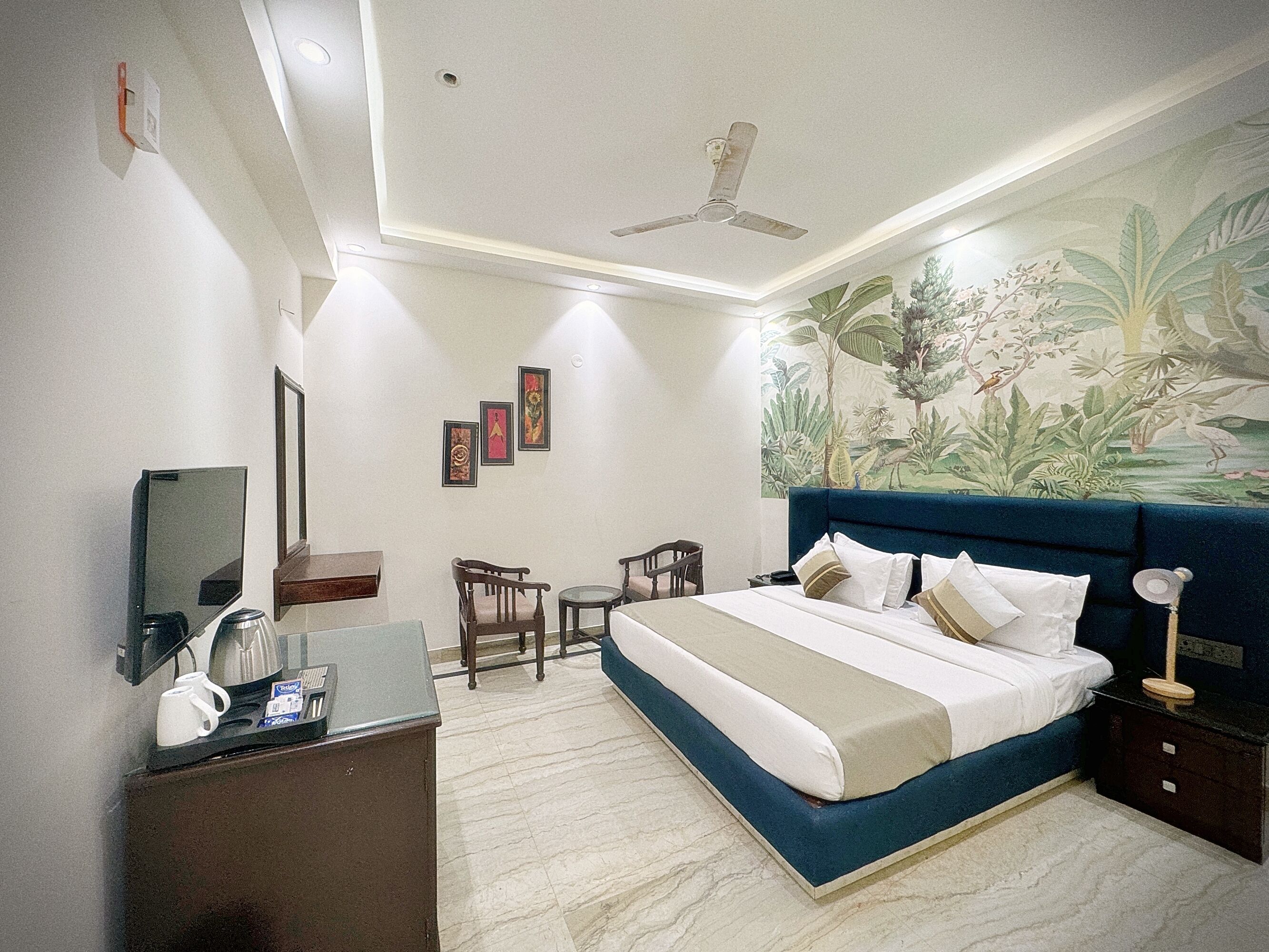 A bedroom with a bed, a desk, a chair, a ceiling fan, and a mural on the wall.