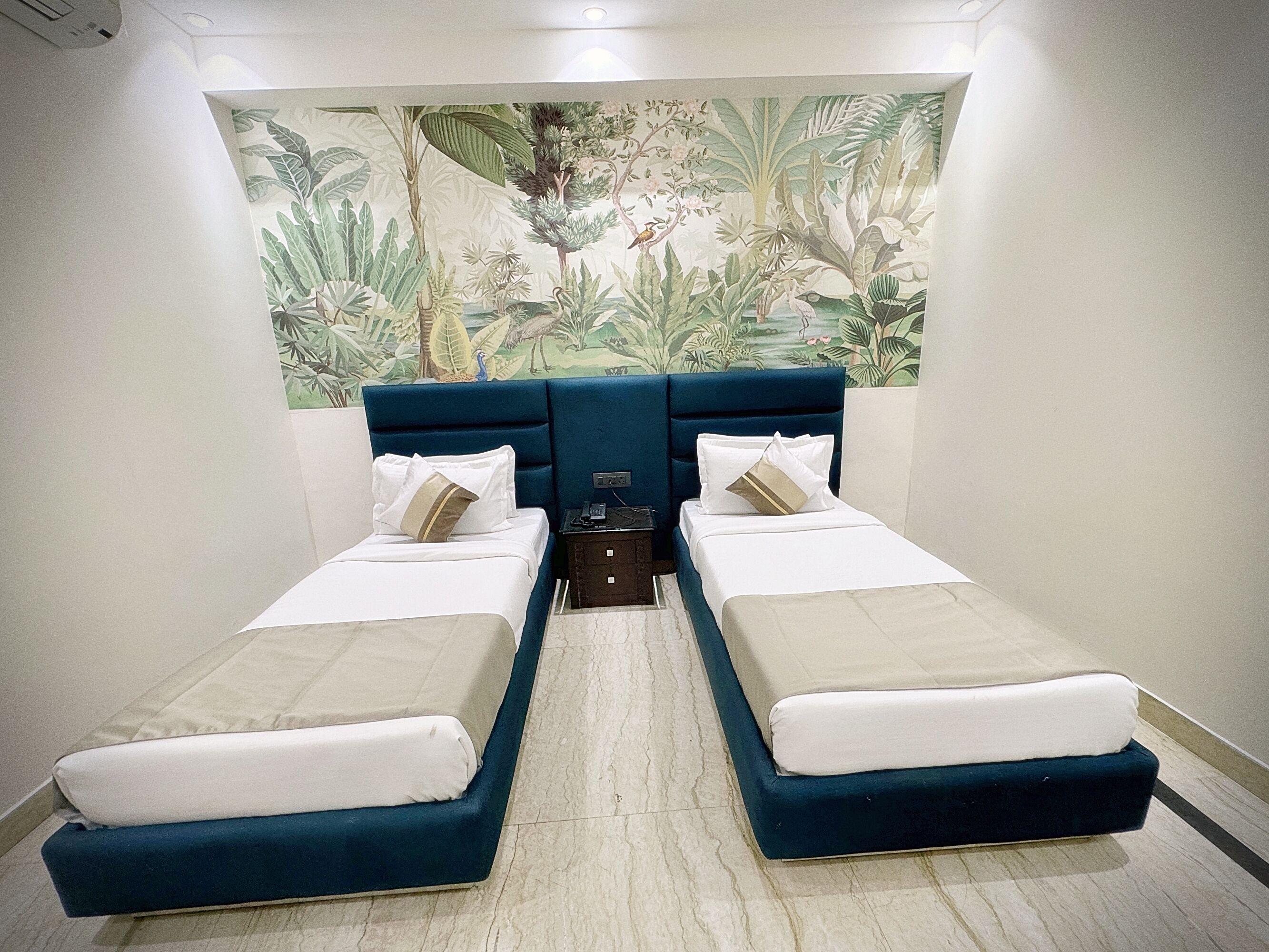 Habitación con dos camas, cada una con cabecera azul, ropa de cama blanca y una mesita de noche con teléfono.