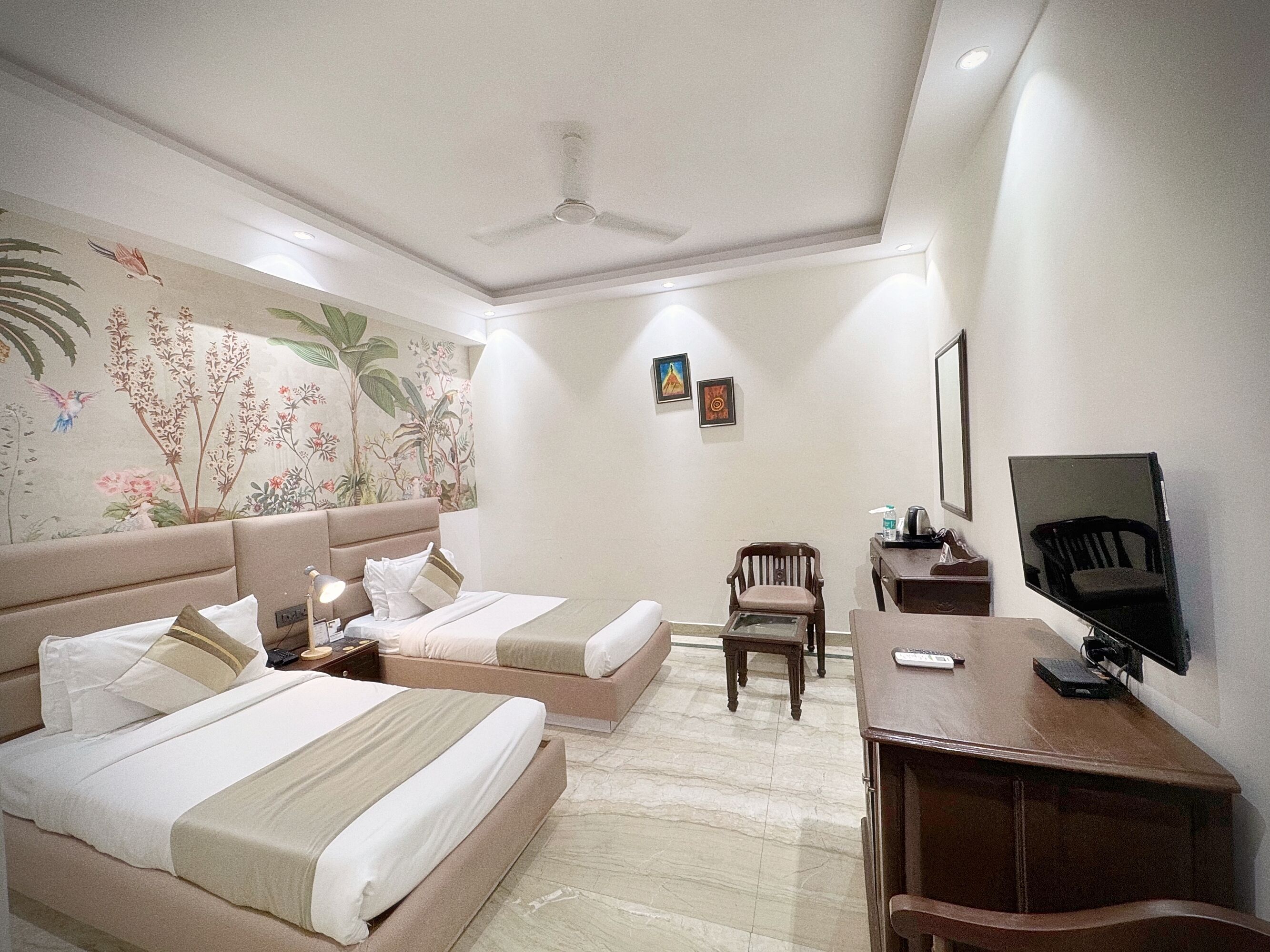 Une chambre d’hôtel avec deux lits, un bureau, une chaise, une télévision et un ventilateur de plafond.