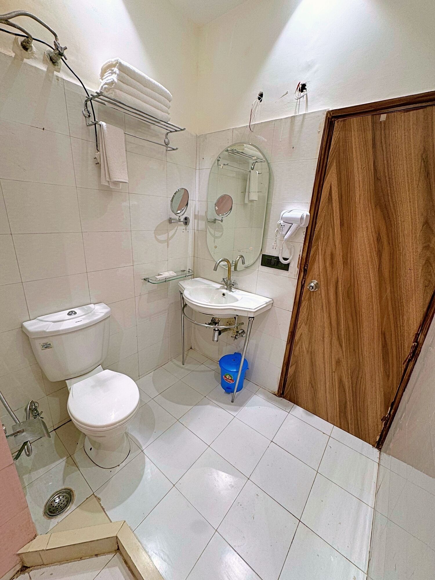 Une petite salle de bain avec des toilettes, un lavabo et un miroir. Il y a un porte-serviettes au-dessus des toilettes et une porte en bois sur la droite.