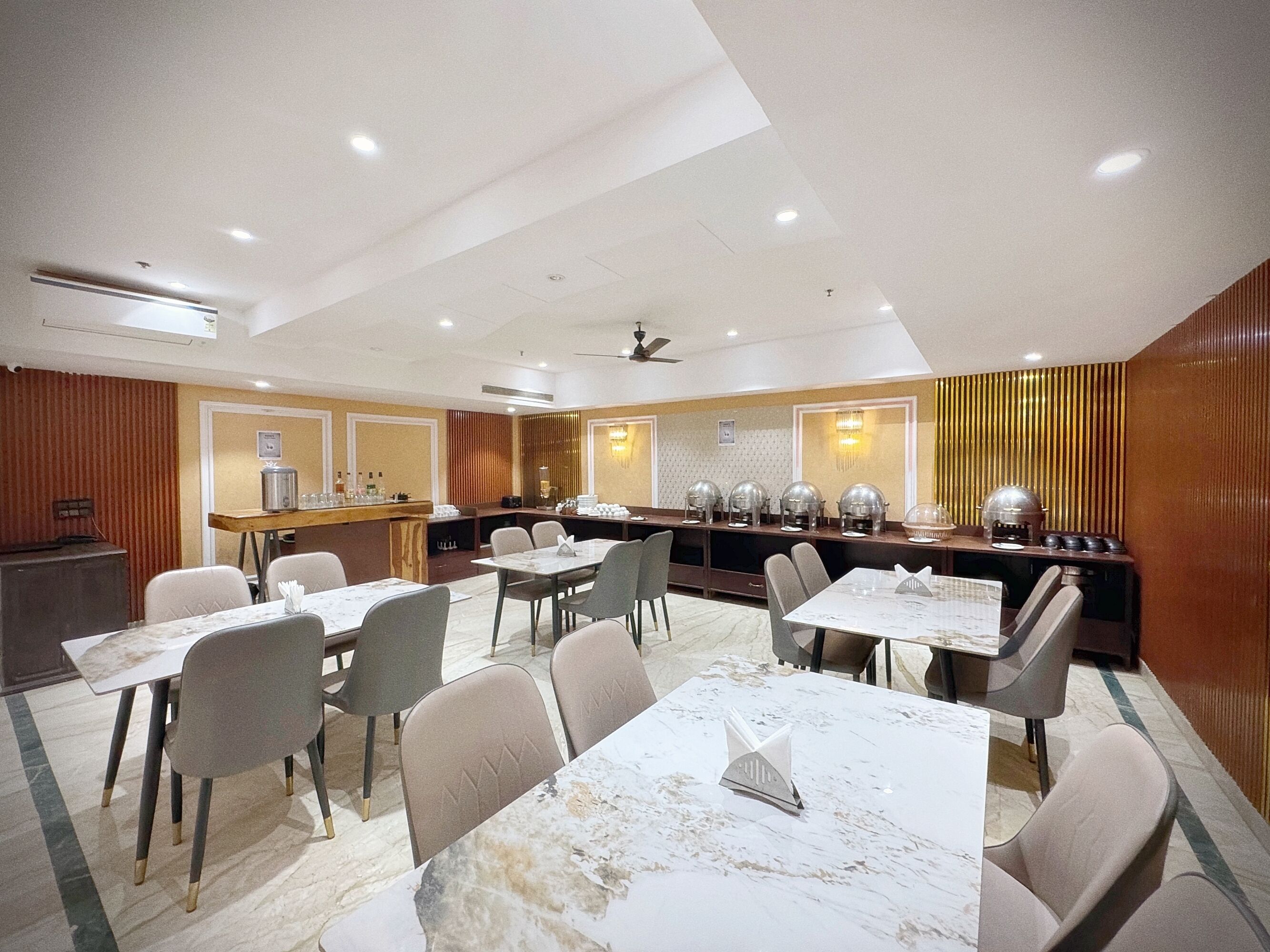 Un comedor de hotel con mesas y sillas, una barra de buffet con equipo de servicio de alimentos y un mostrador con caja registradora.