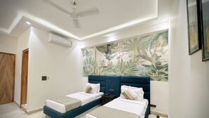 Una camera d'albergo con due letti, una ventola a soffitto, un grande murale tropicale e una porta in legno.