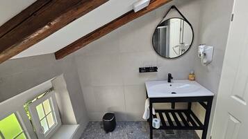 A small, modern bathroom with a white sink, a mirror, and a black vanity. There is a window with frosted glass and a view of greenery outside.