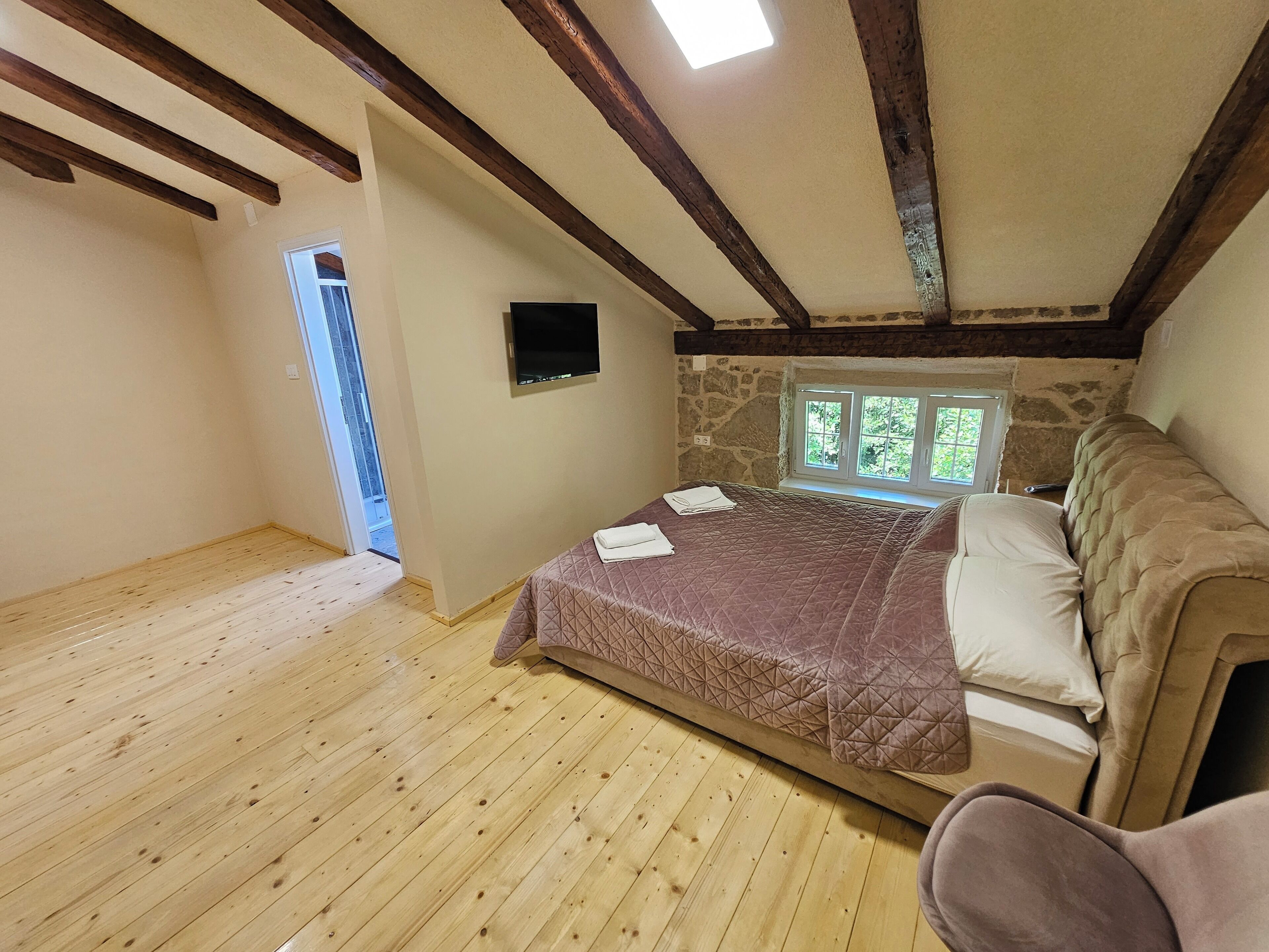 Ein Schlafzimmer mit Holzboden, einem Bett mit gesteppter Decke, einer Steinsäule und einem Fenster mit Blick ins Grüne.