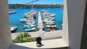 A view through an arched window of a marina with boats docked, a clear blue sky, and a distant shoreline. - Villa Gaj (Omisalj)